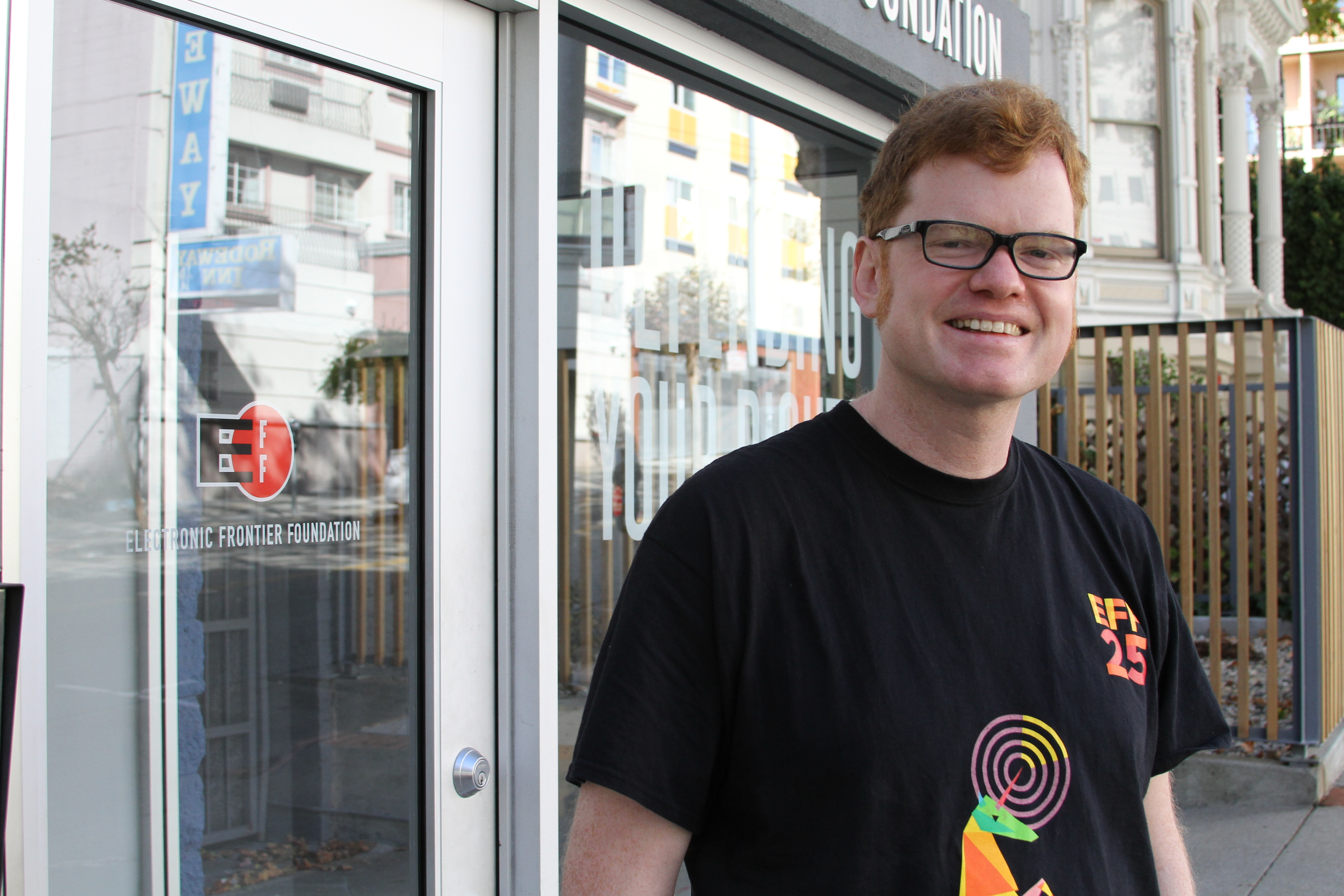 A photo of Elliot smiling, wearing a black shirt with a rainbow unicorn and the text "EFF25".
